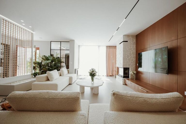Open-plan living room with bouclé sofas, a travertine coffee table and a white stone fireplace.